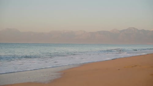Morgendämmerung am Sandstrand. Die Sonne beleuchtet die Berge in der Ferne vom Meer
.