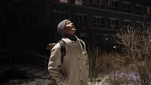 Man Enjoying Snowfall Outside Building at Night