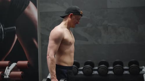 Strong male with naked torso do standing dumbbell biceps curl at indoor gym