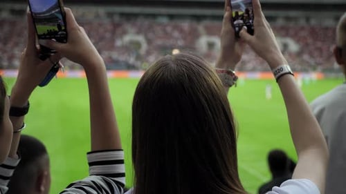 Una vista desde la espalda de mujeres en las gradas de un estadio donde toman fotos