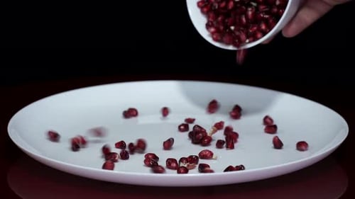 Pomegranate Seeds Falling Onto a White Plate