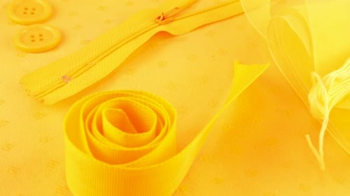 Cotton fabric and various sewing accessories in merigold yellow colors rotates on the showcase.