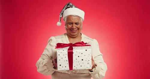 Christmas, gift and shake with face of old woman in studio for announcement
