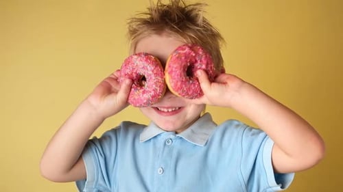 Happy Child Holding Glazed Donut Little Boy is Covering Eyes Donuts on Yellow Studio Background Kid