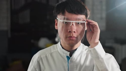 Chemical Engineer Adjusting Protective Glass in Illuminated Workshop