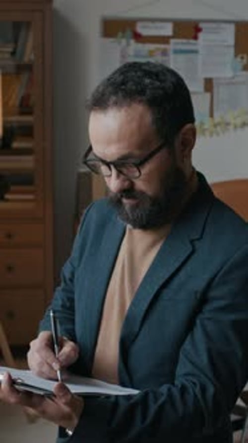 Man with Beard Writing on Clipboard in Office