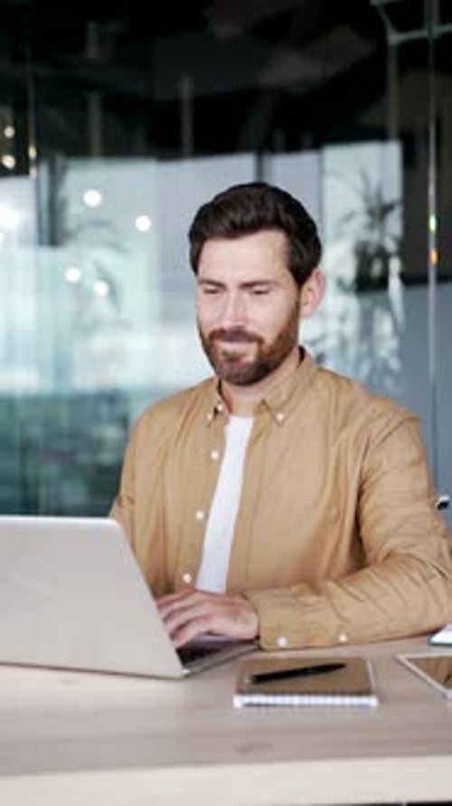 Happy handsome businessman working on a laptop computer sitting at workplace in business office.