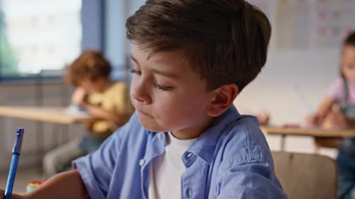 Young Student Writing at School Desk in Classroom
