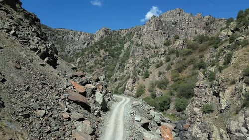 Low aerial tracks narrow gravel road in bottom of rugged rock gorge