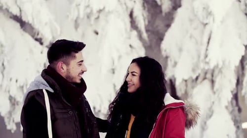 Young couple talking in snowy winter forest outdoors enjoying a peaceful walk