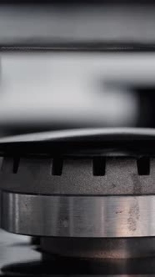 Close-up shot of a clean gas burner on a black stove with a pot placed on it, and the fire ignites.