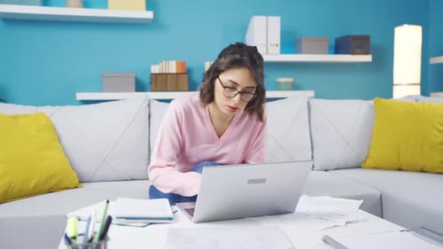 Junge Frau, die von zu Hause aus arbeitet, macht sich Notizen, arbeitet am Laptop.