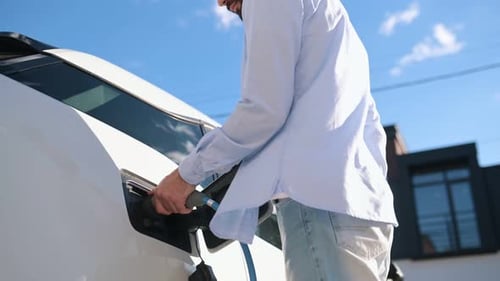Man Charging Electric Car Outside on Sunny Day