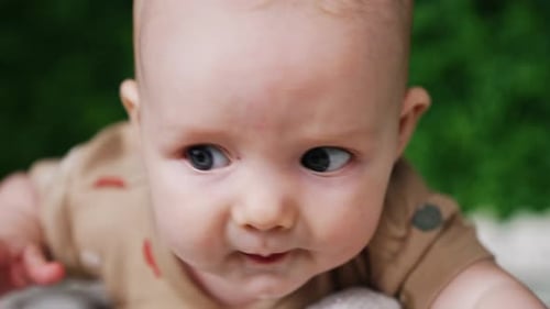Face of a sweet little Caucasian infant. Close up. Lovely grey-eyed baby looking up with surprise.