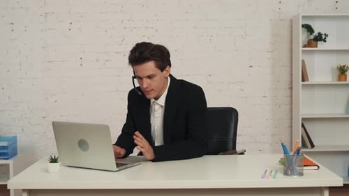 Medium Video of a Young Man in an Office Wearing a Call Center Headset Talking to Somebody Working