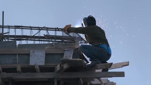 Welder welds iron bars on of house at a construction site, background. Welding at heights.