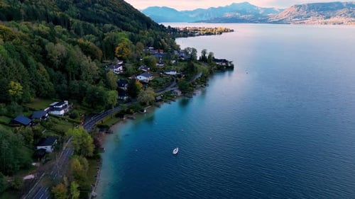 Ein türkisfarbener See, umgeben von üppigen grünen Bergen, mit einem Segelboot und mehreren Häusern am Ufer