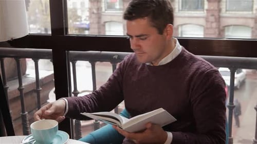 Man Enjoys Reading a Book While Sipping Coffee at a Cozy Cafe