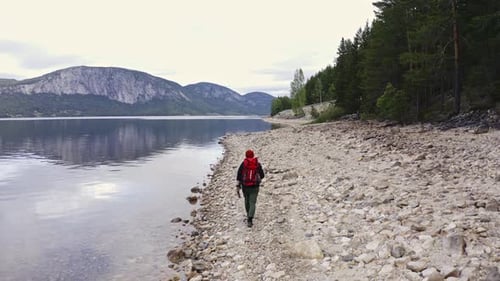 Guy Traveler Walks Along the Shore with a Backpack Along a Beautiful Lake