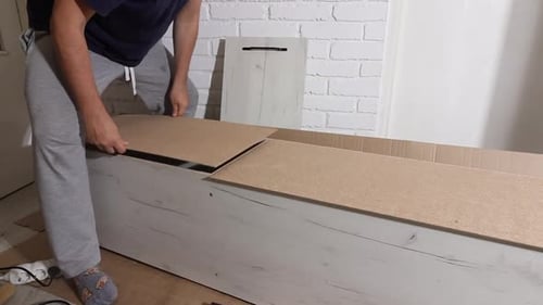 L'homme répare le mur arrière de l'armoire. À l'aide de clous. Meubles à assembler soi-même.
