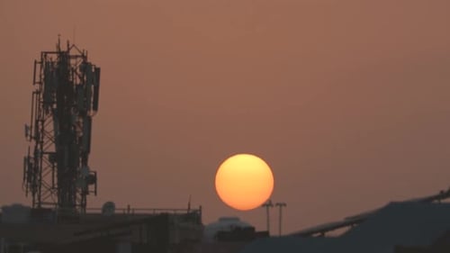 Timelapse of sun setting behind residential buildings and a mobile tower during evening sunset time