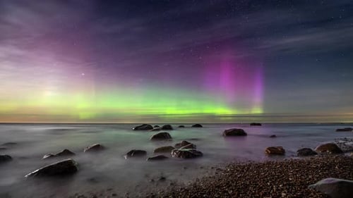 Timelapse. Scenic seashore with a boulders under a starry night sky with the northern lights.