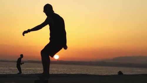 Silhouette of a Man Skating on a Longboard at Bright Orange Sunset By the Ocean