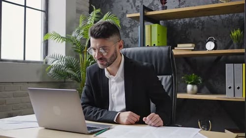 Smiling Businessman Talks Via Video Call on Laptop in Office