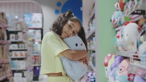 A Young Girl Joyfully Explores a Colorful Toy Store Holding Her Favorite Plush Toy Tightly