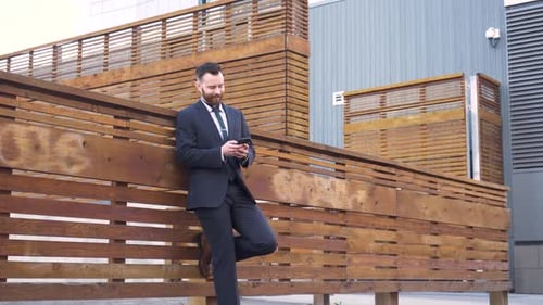 Man in suit using phone outdoors by wood wall