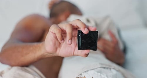 Main, préservatif et personnes au lit à des fins de protection, de relations sexuelles et de contraception avec luxure