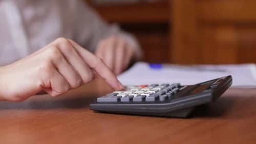 Person Using Calculator and Writing on Paper