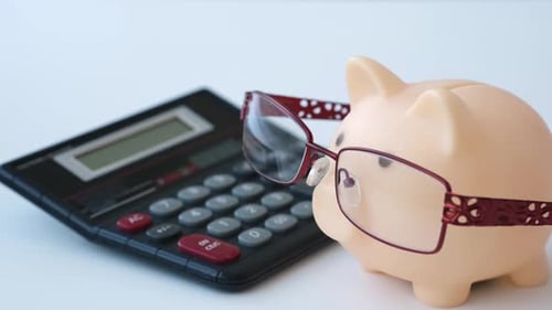 Main mettant des pièces dans une tirelire dans des verres à côté de la calculatrice sur une table blanche