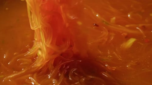 Noodles Being Stirred in Orange Asian Soup