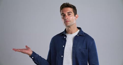 Face, smile and offer with the palm of a man in studio isolated on gray background to show space