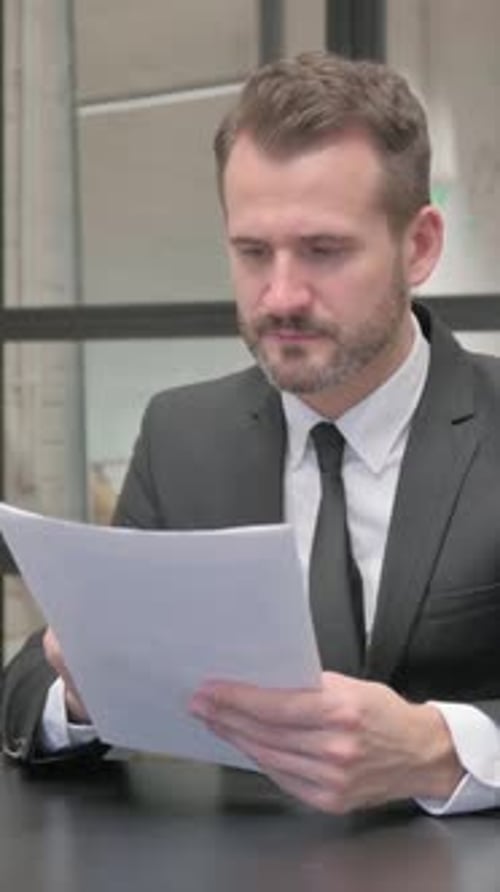 Serious Businessman Reviewing Documents at Office Desk