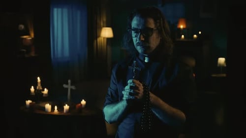 Priest Praying with Rosary Beads in Candlelit Room
