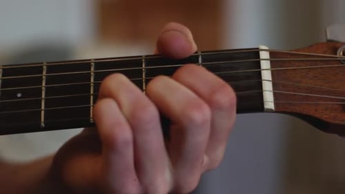 A close up of a young man is playing guitar, the camera pans left to show his strumming hand.