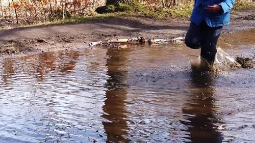 Children, of African ethnicity, running and splashing in a large puddle of water for fun. Slow moti