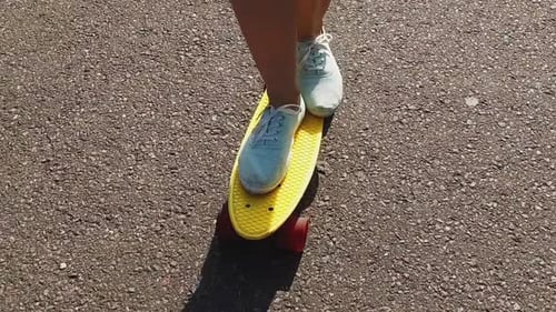 Teenage girl feet riding cruiser skateboard on urban road in slow motion mode