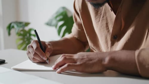 Man Writing in a Notebook at Bright Desk