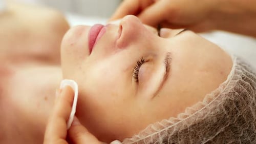 Beautician cosmetologist cleanses the skin of face with cotton pad disk in a beauty clinic salon.
