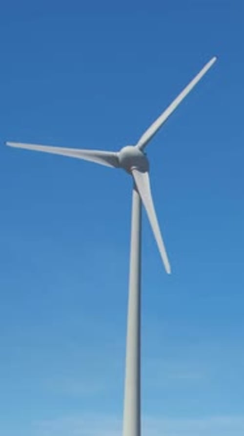 Close shot of wind turbine rotating against clear blue sky on sunny day