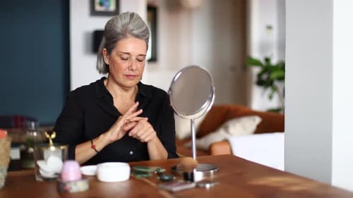 Woman Applying Moisturizer at Table with Mirror Indoors