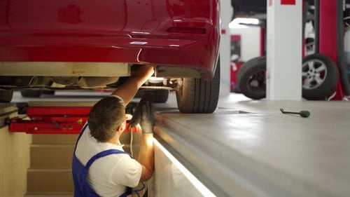 Auto Mechanic Inspects Suspension on Red Car at Vehicle Service Center Using Hydraulic Lift