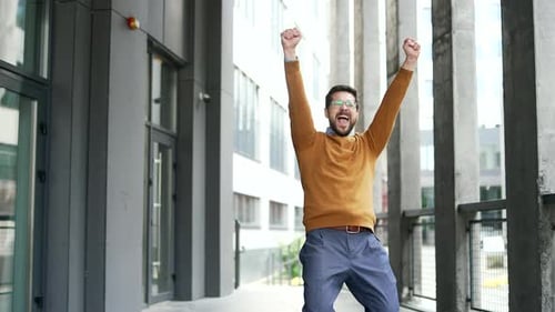 Happy excited businessman celebrating success standing outside office building. Joyful manager