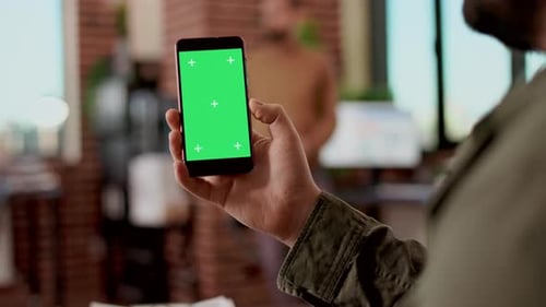 Person Holding Smartphone with Green Screen in Office