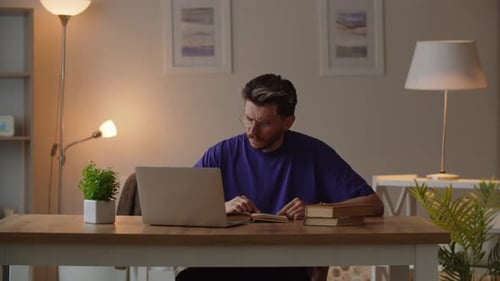 Young Adult Reading Book with Laptop at Desk