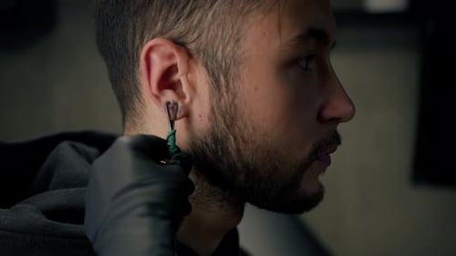 Tattoo piercing studio - a woman makes an ear piercing to a man to a guy