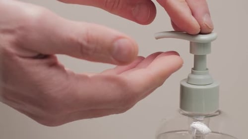 Close up of male hands pushing on a dispenser with liquid transparent soap to wash hands on a white
